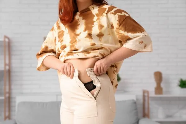 Image of woman trying to do her trousers up after pregnancy weight gain Biggleswade