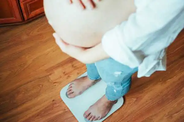 Image of woman weighing herself and experiencing weight gain through pregnancy Biggleswade